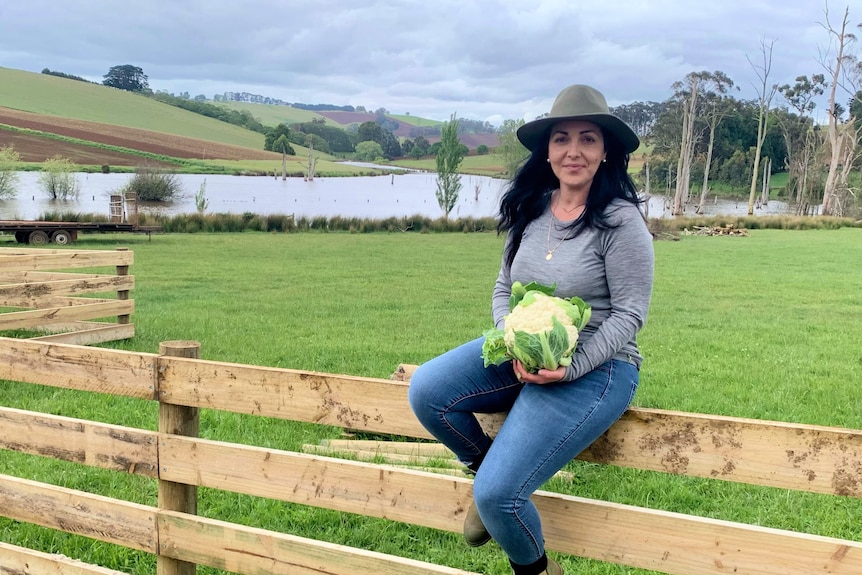 Emma Germano sits on her fence and holds a head of cauliflower at her Mirboo North farm