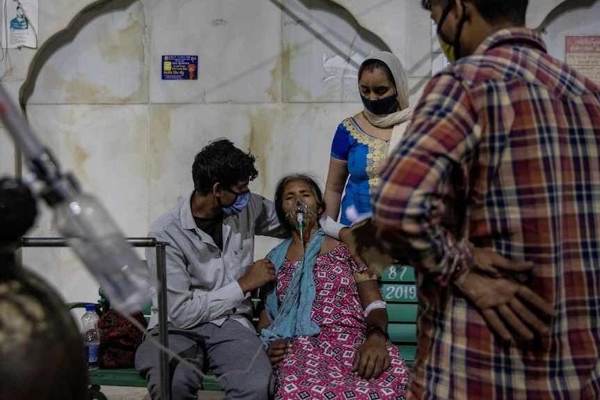 A man cradles a woman who is receiving oxygen while another man and woman watch on. 