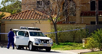 A police car in front of a big house roped off by crime tape.