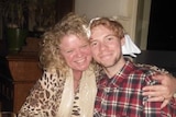 A woman with curly blonde hair wearing a leopard print shirt, with her arm around a young man with strawberry blond hair.