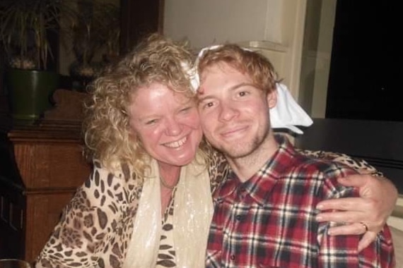 A woman with curly blonde hair wearing a leopard print shirt, with her arm around a young man with strawberry blond hair.