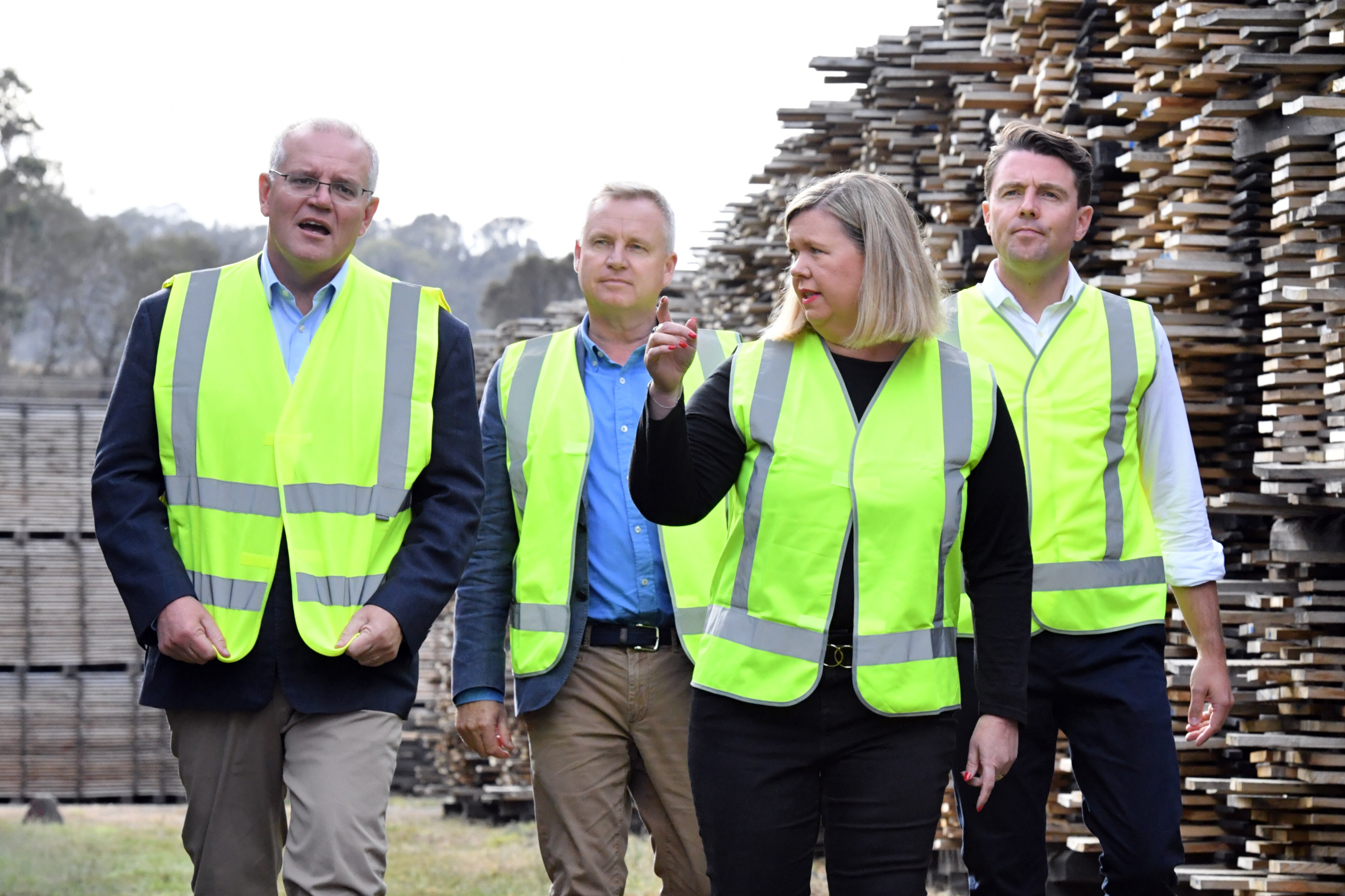 Three people in high-visibility vests walk through a lumberyard