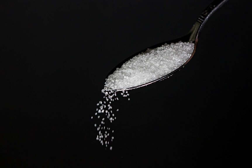 A metal spoon spills sugar