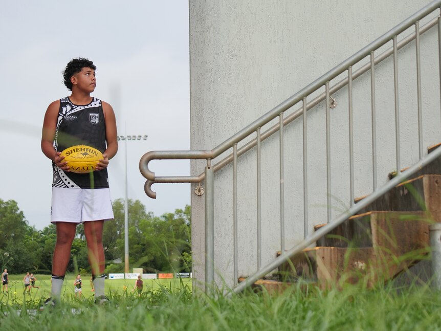 A boy holds a footy and looks up some stairs to his left