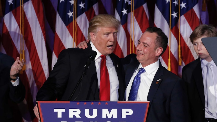 Donald Trump (L) and Reince Priebus (R) stand embracing at a podium at a rally