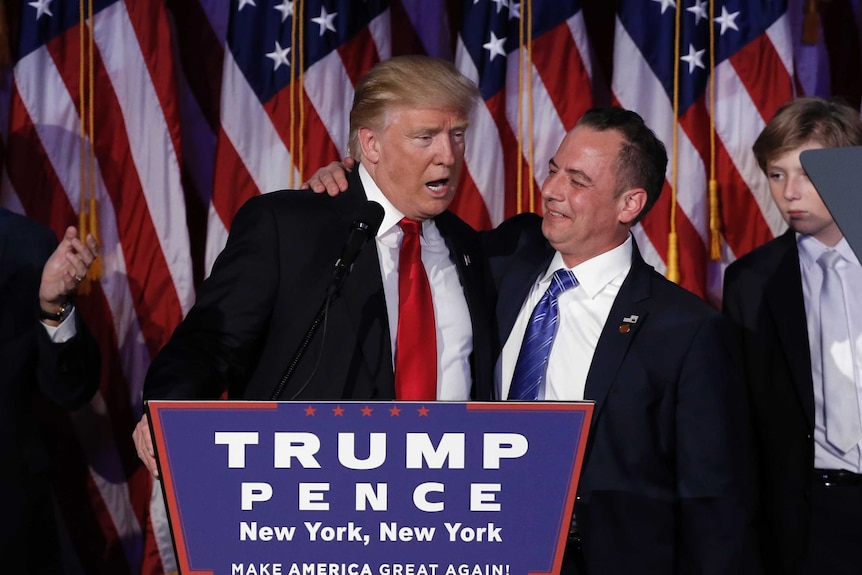 Donald Trump (L) and Reince Priebus (R) stand embracing at a podium at a rally