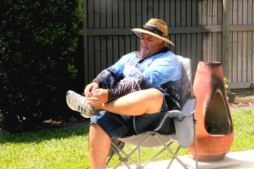 Greg Jude sitting in a deck chair in his backyard tying his left shoe.