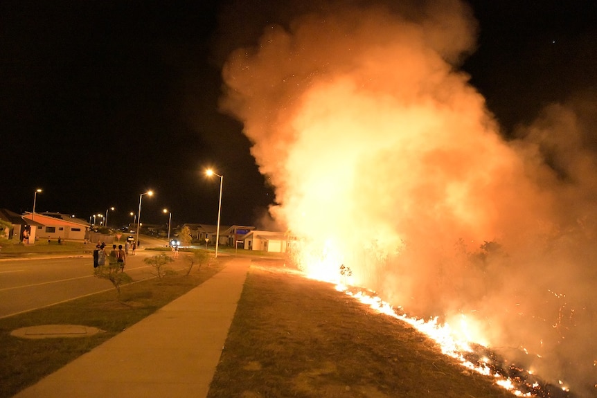 A fire spreads in Zuccoli as people watch on from the sidewalk.