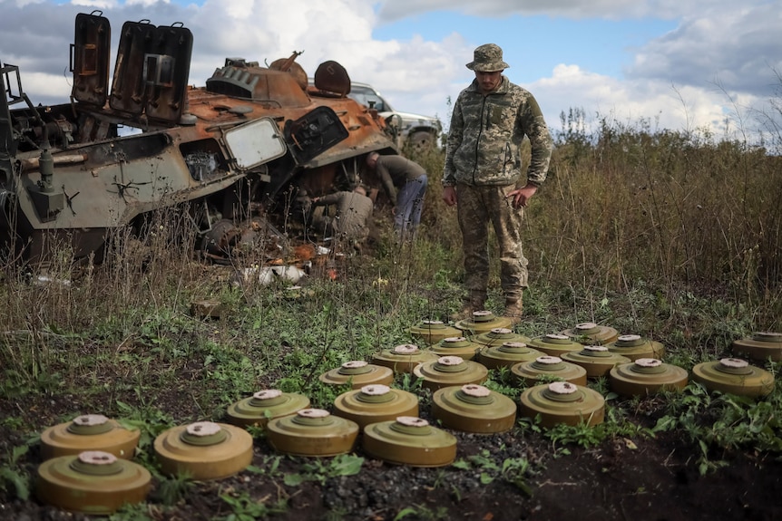 A Ukrainian serviceman is examining anti tanks mines near a destroyed vehicle.