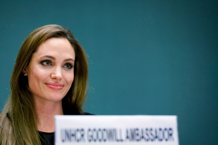 The actress Angelina Jolie sits at a desk.