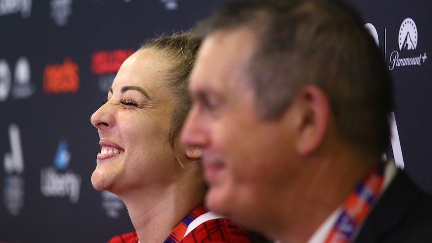 A soccer player wearing red grins and closes her eyes during a press conference