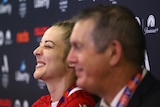 A soccer player wearing red grins and closes her eyes during a press conference