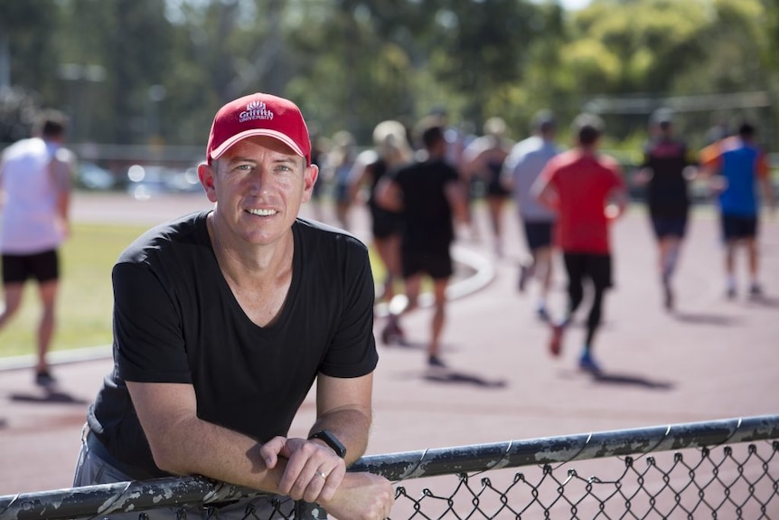 Man leaning against fence with runners in the background