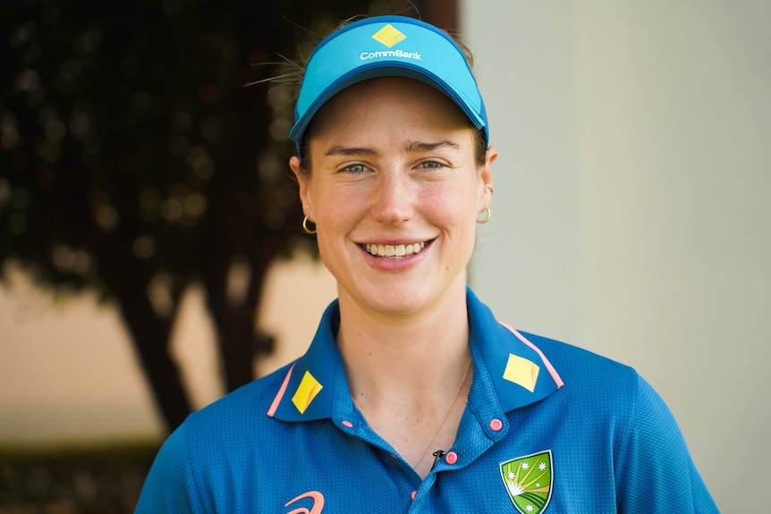 A close up of a woman with green eyes smiling while wearing a blue cap and top.