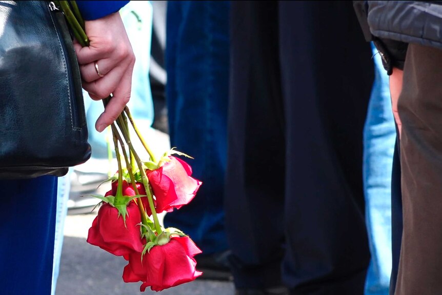 A woman holds roses by her side in a crowd of people.
