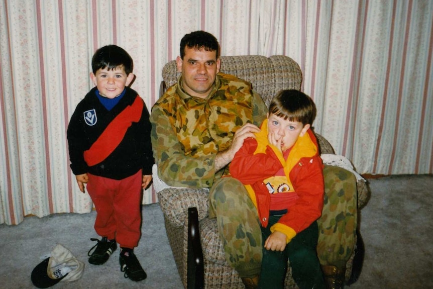Ash Morris with his father Ricky and his brother pose for a photo in a lounge room.