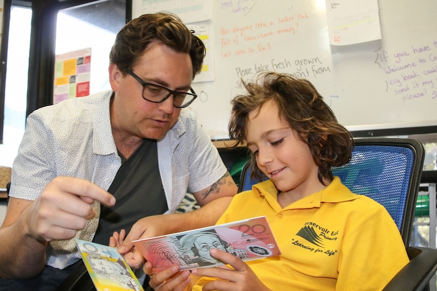 Tim Norton talks to his son Avery Norton about how to save pocket money in the classroom of his primary school.