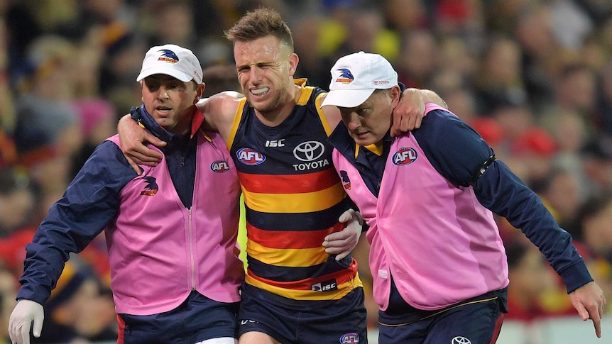 A football player limps off the field with the help of two trainers.