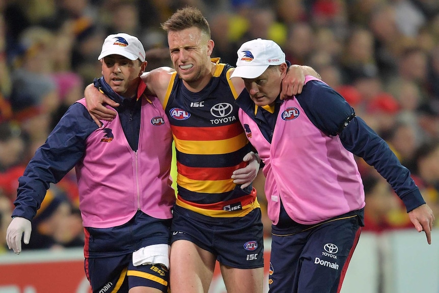 A football player limps off the field with the help of two trainers