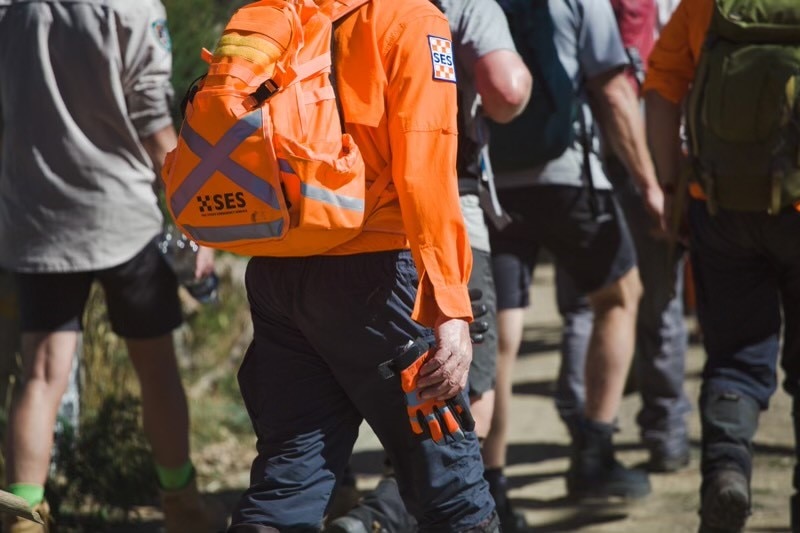 A close up of an SES volunteer in orange holding their glove in their hand as they walk with crews.