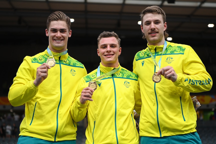 Three male athletes wearing yellow and green hold up gold medals
