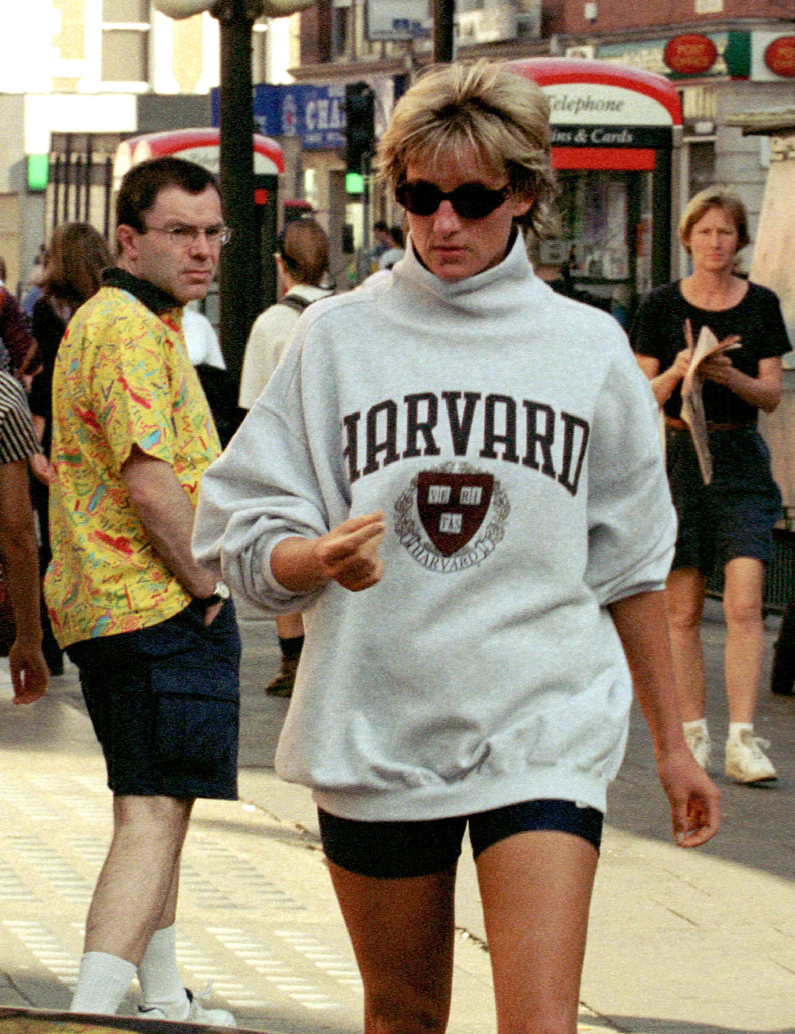 Princess Diana wearing a pair of dark bike shorts, sunglasses and a bag grey Harvard jumper