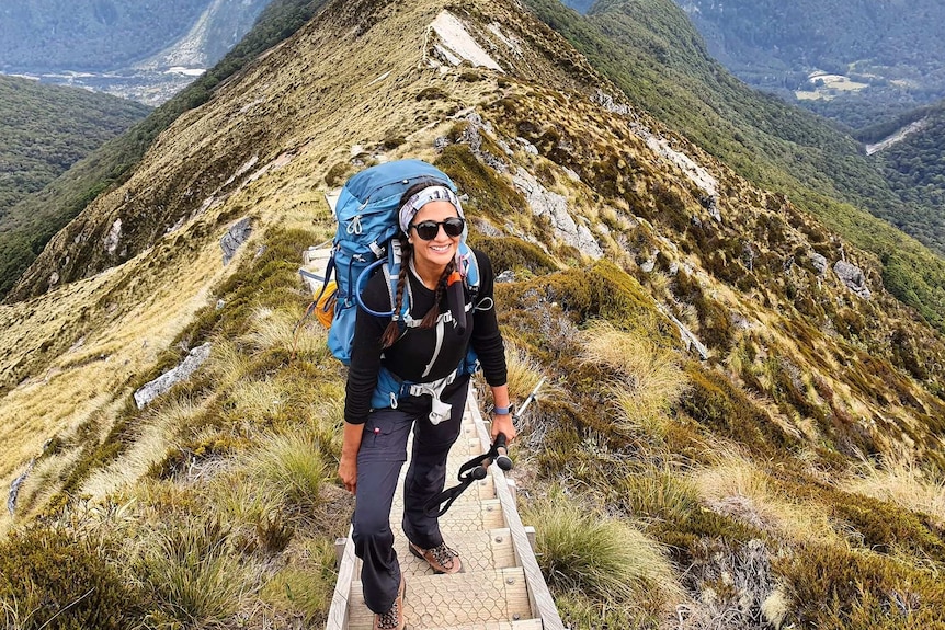 Sharmali Kulatunga stands on stairs with her backpack and walking poles on the Kepler Trail in New Zealand.