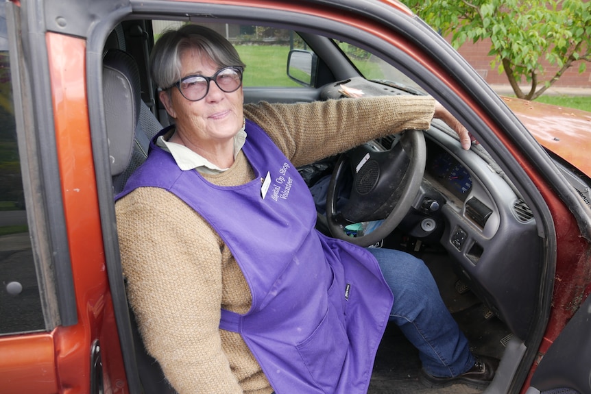 A woman in a purple apron sits in the driver's seat of her ute.