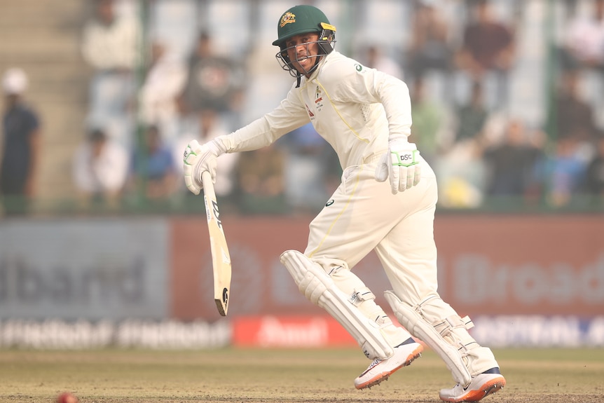 An Australian male batter looks to his left as he watches the progress of a shot.