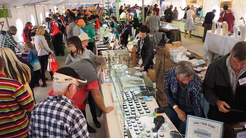 People stand in a large tent looking at market stalls showing gems and jewellery.