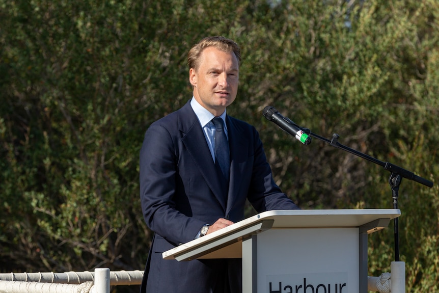 a man standing behind a microphone outdoors giving a speech