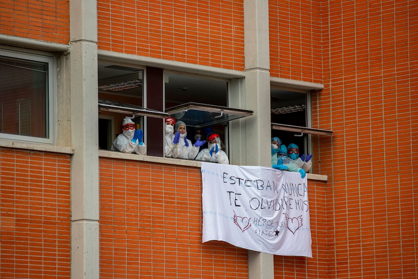 Health workers pictured applauding inside an open window  during a memorial for their co-workers in Spain.
