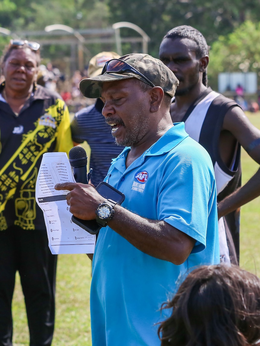 Willie Rioli Senior speaking with a microphone at a football oval.