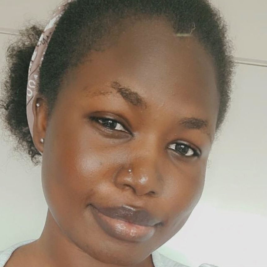 A woman with her nose pierced and her hair pulled back looks straight at the camera.