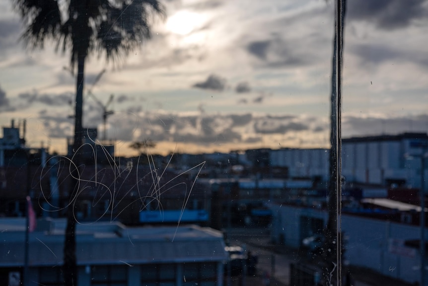 Low set buildings and shops behind a glass window that has been scratched with graffiti.