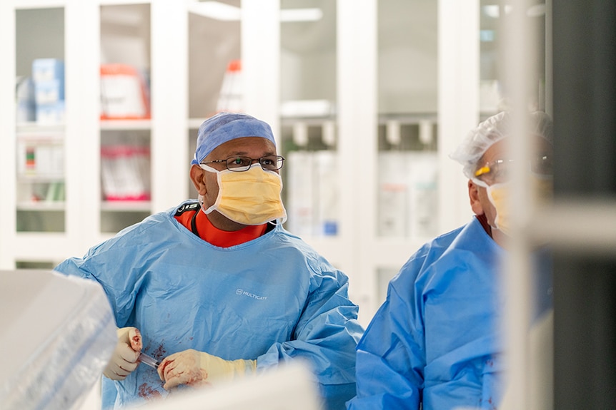 A man in scrubs performing surgery.