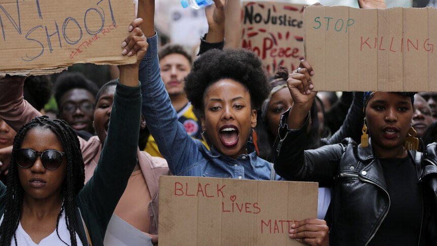 A woman holding a Black Lives Matter sign gives the Black Power salute during a protest.