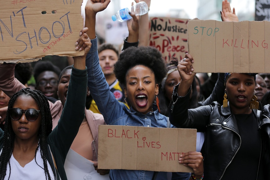 A woman holding a Black Lives Matter sign gives the Black Power salute during a protest.