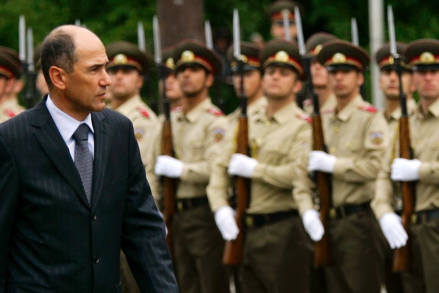 Janez Jansa walking past a row of Slovenian soldiers holding rifles