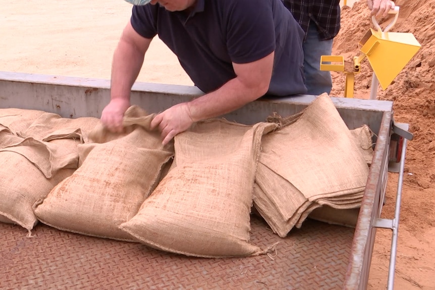 A man loading filled sandbags into a trailer