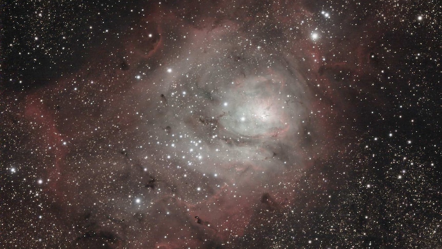 A white and red-tinged cluster in a night sky crowded with stars.