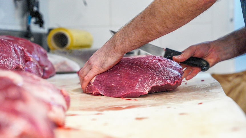 Butcher slices through beef with beef piled high in foreground