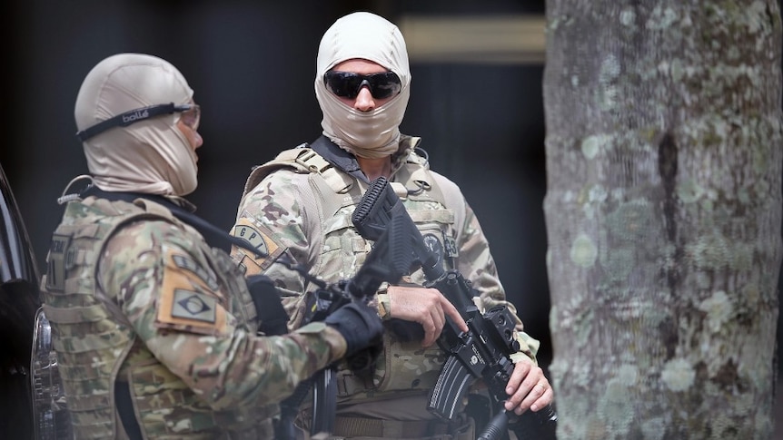 Brazilian federal police stand guard, their faces covered in masks and with guns.