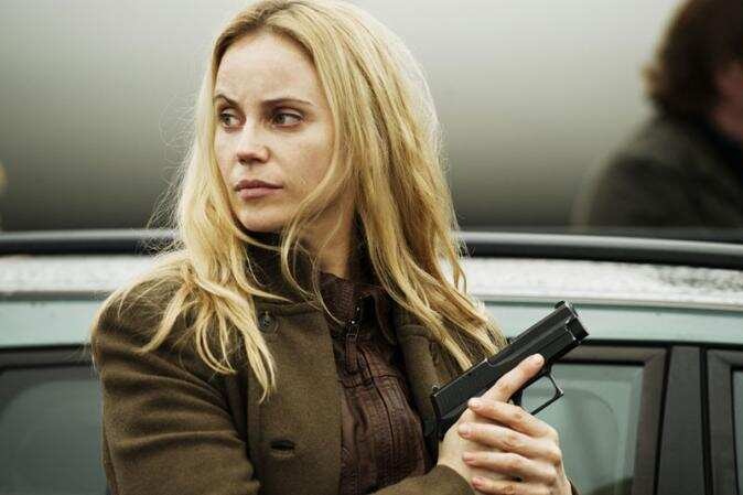 A woman with blond hair holds a pistol 