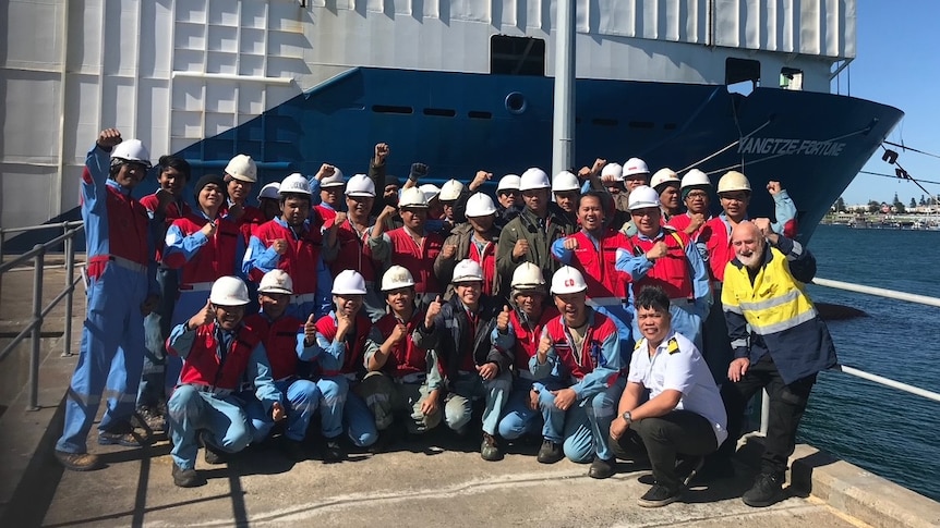 Ship crew members in hard hats and high vis vests on the dock.