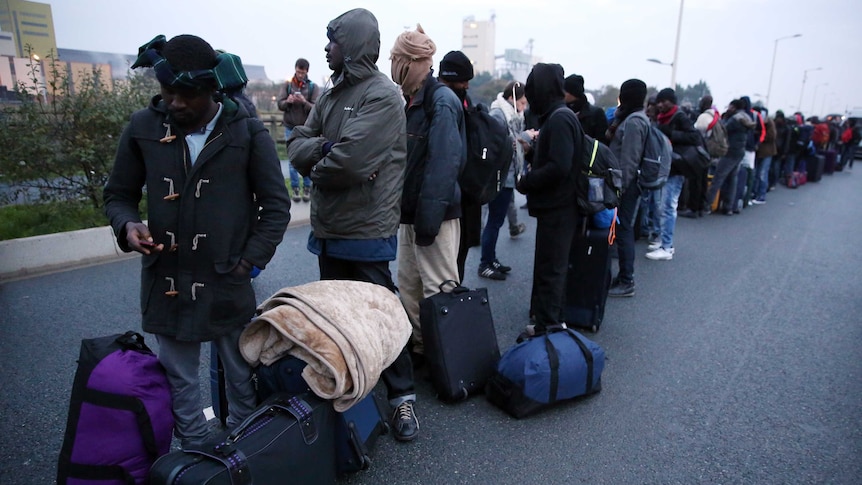 Asylum seekers with their belongings queue at the start of their evacuation.