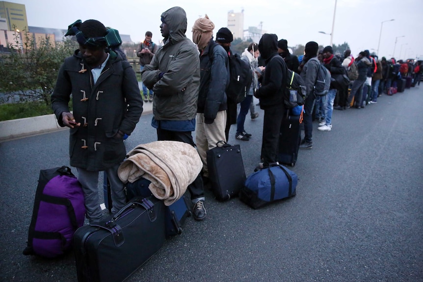 Asylum seekers with their belongings queue at the start of their evacuation.