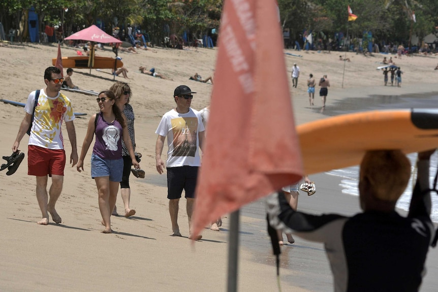 Tourists in beach wear stroll along Kuta Beach