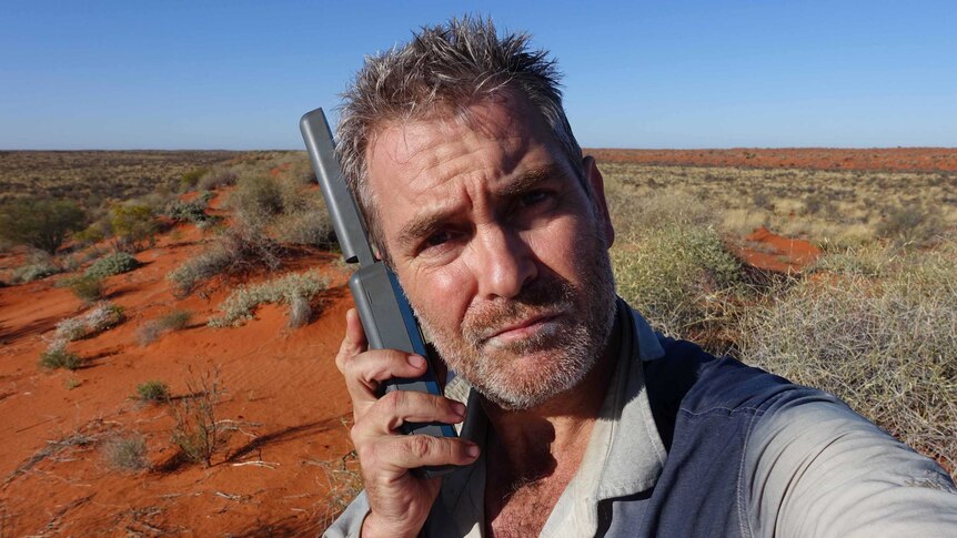 A man on a satellite phone in a desert.
