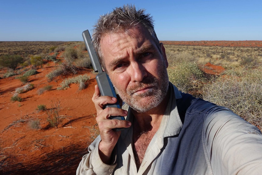 A man on a satellite phone in a desert.